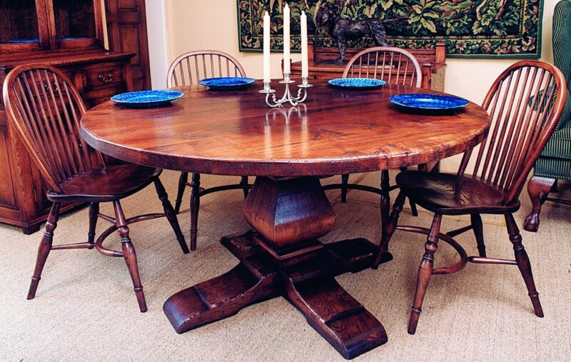 Round pedestal dining table with hoop-back chairs laid for dinner in a panelled dining room